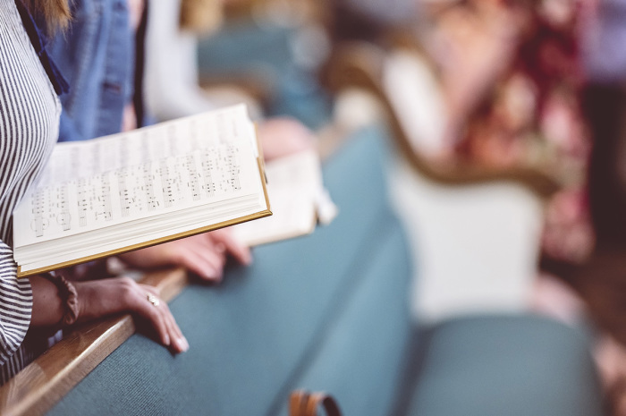 People stand in the church pews while holding a hymnal. 